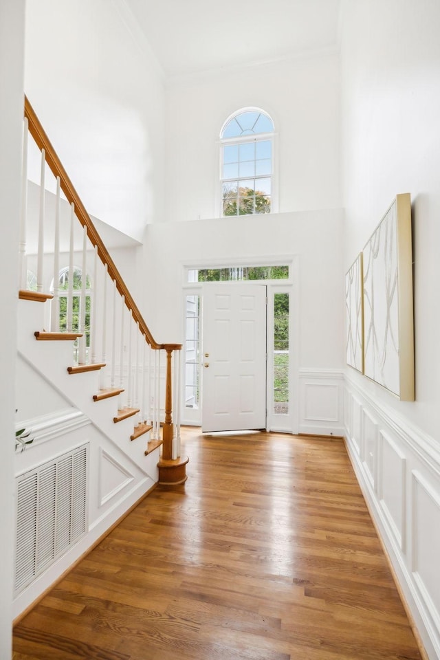 entryway featuring hardwood / wood-style floors, crown molding, and a high ceiling