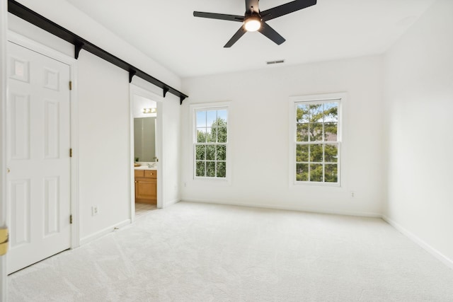 unfurnished bedroom featuring connected bathroom, light colored carpet, a barn door, and ceiling fan