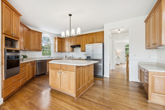 kitchen with a kitchen island, appliances with stainless steel finishes, backsplash, hanging light fixtures, and light hardwood / wood-style flooring