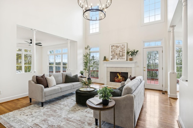 living room with ornate columns, hardwood / wood-style floors, a tiled fireplace, a high ceiling, and ceiling fan