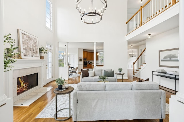 living room with a tiled fireplace, a high ceiling, light wood-type flooring, and a chandelier