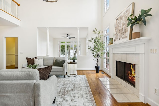 living room featuring ornate columns, light hardwood / wood-style flooring, a tile fireplace, a towering ceiling, and ceiling fan