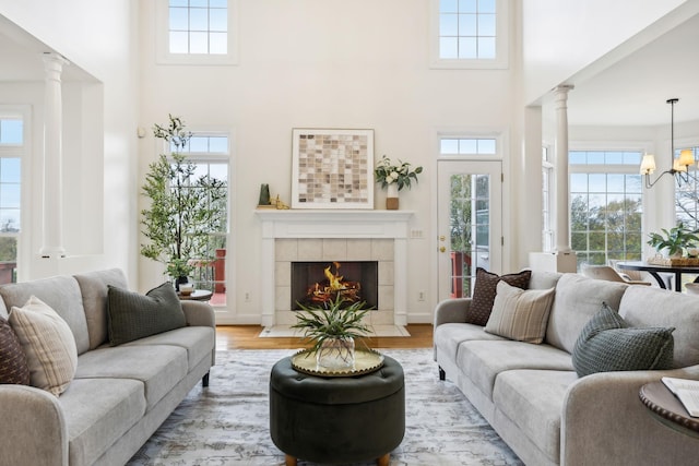 living room with a towering ceiling, light hardwood / wood-style floors, a tile fireplace, and ornate columns