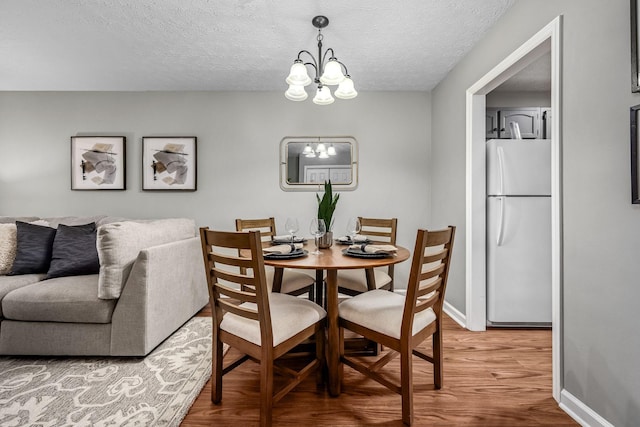 dining area with wood-type flooring, a textured ceiling, and a notable chandelier