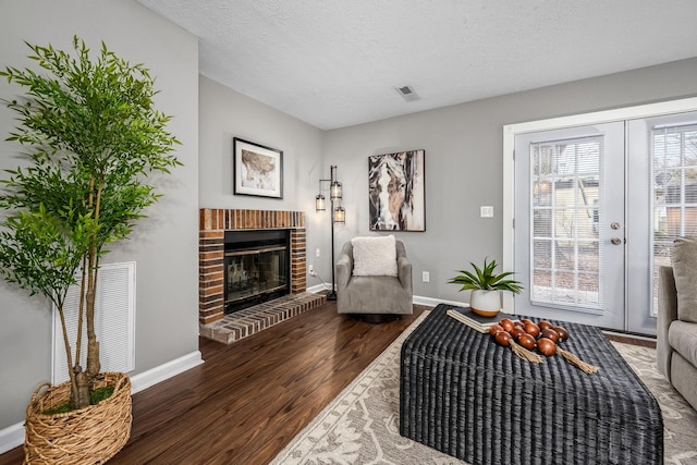 sitting room with a brick fireplace, a textured ceiling, dark hardwood / wood-style flooring, and french doors