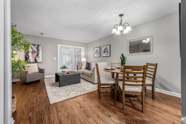 dining area featuring hardwood / wood-style flooring, an inviting chandelier, french doors, and a textured ceiling