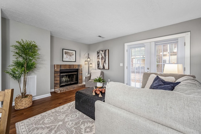 living room with a brick fireplace, dark wood-type flooring, french doors, and a textured ceiling