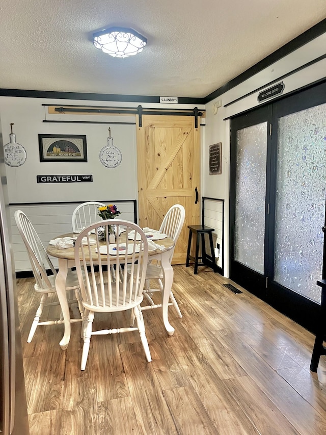 dining space featuring hardwood / wood-style flooring, a barn door, and a textured ceiling