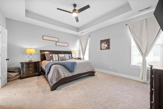 bedroom featuring ceiling fan, a tray ceiling, and light carpet