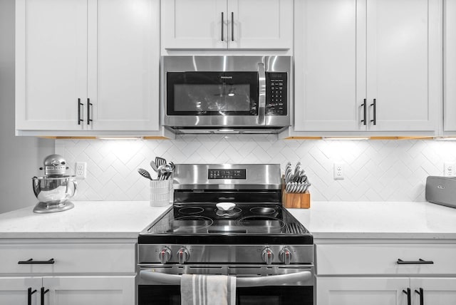 kitchen featuring stainless steel appliances, light stone countertops, white cabinets, and decorative backsplash