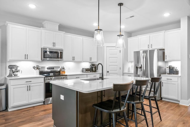 kitchen with sink, decorative light fixtures, an island with sink, stainless steel appliances, and white cabinets