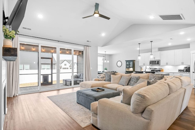 living room featuring high vaulted ceiling, ceiling fan with notable chandelier, and light hardwood / wood-style flooring