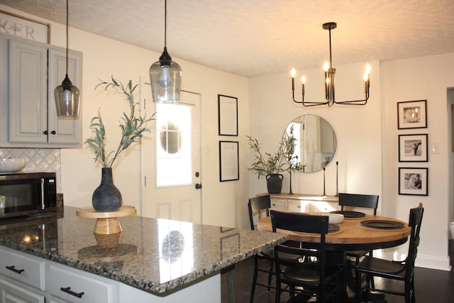 kitchen featuring backsplash, dark stone counters, decorative light fixtures, and gray cabinetry