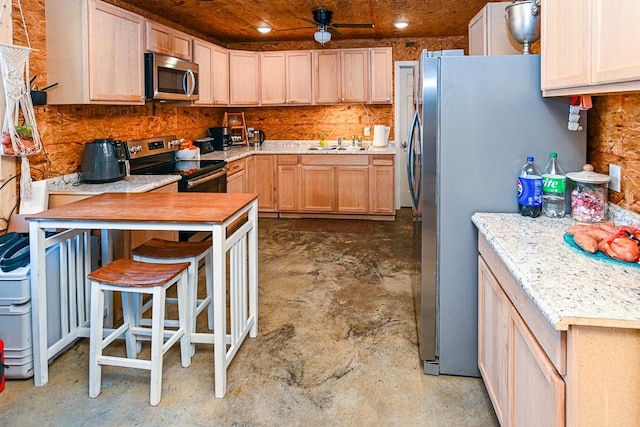 kitchen with sink, light stone counters, light brown cabinets, appliances with stainless steel finishes, and ceiling fan