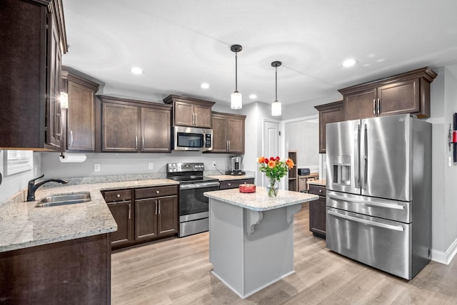 kitchen featuring sink, light stone counters, a center island, appliances with stainless steel finishes, and pendant lighting