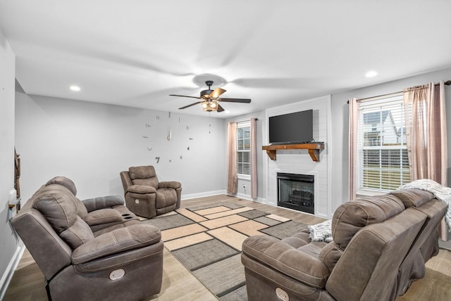 living room with a large fireplace, ceiling fan, and light wood-type flooring