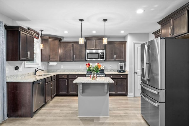 kitchen with a kitchen island, appliances with stainless steel finishes, decorative light fixtures, sink, and light hardwood / wood-style floors