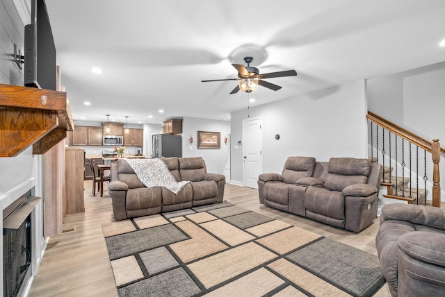 living room featuring a fireplace, ceiling fan, and light wood-type flooring