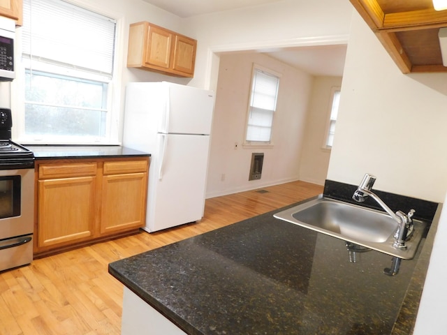 kitchen with sink, dark stone countertops, stainless steel appliances, a wealth of natural light, and light hardwood / wood-style floors