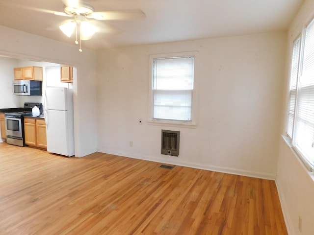 kitchen with appliances with stainless steel finishes, light brown cabinetry, heating unit, and light wood-type flooring