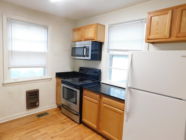 kitchen with a healthy amount of sunlight, appliances with stainless steel finishes, heating unit, and light hardwood / wood-style flooring