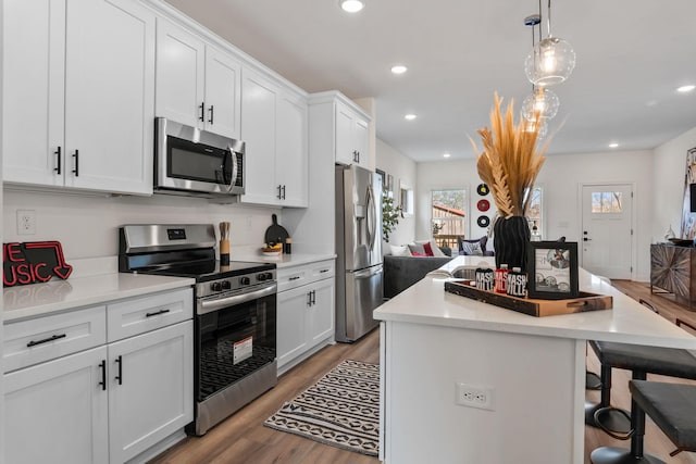 kitchen with stainless steel appliances, light hardwood / wood-style floors, white cabinets, a kitchen island, and decorative light fixtures