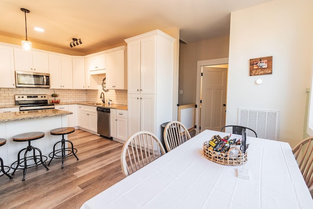 kitchen featuring appliances with stainless steel finishes, tasteful backsplash, white cabinets, hanging light fixtures, and light stone countertops