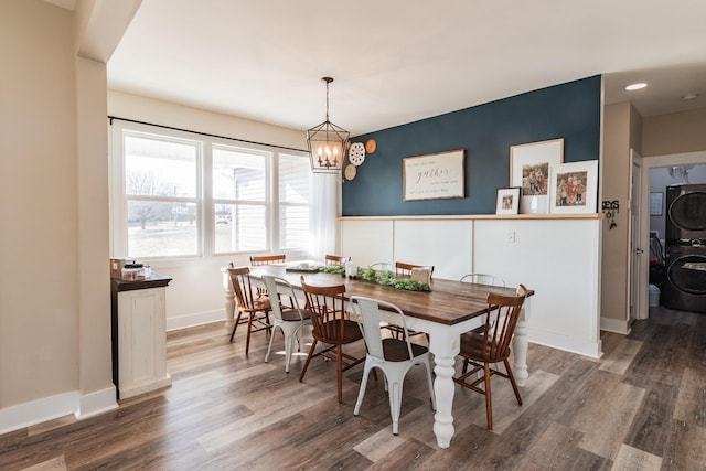 dining space with dark wood-type flooring, stacked washing maching and dryer, and a notable chandelier