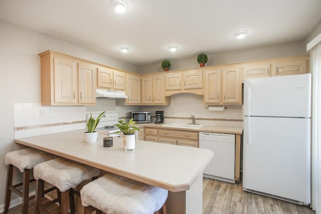 kitchen with sink, white appliances, light hardwood / wood-style flooring, a breakfast bar, and light brown cabinetry