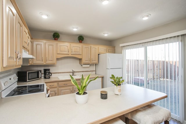 kitchen featuring sink, white appliances, a kitchen bar, kitchen peninsula, and light brown cabinets