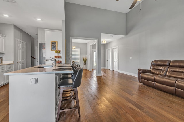 kitchen with dark wood-type flooring, sink, a breakfast bar area, white cabinetry, and ceiling fan