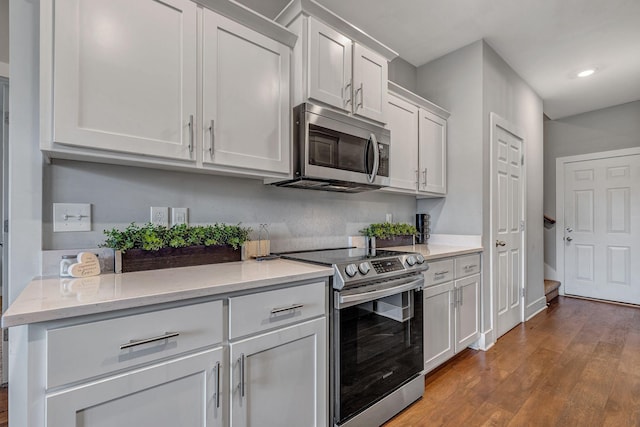 kitchen with light stone counters, hardwood / wood-style floors, white cabinets, and appliances with stainless steel finishes