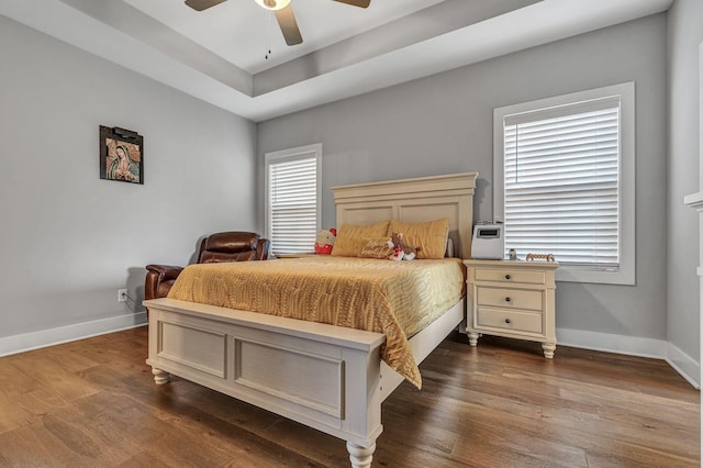 bedroom with dark wood-type flooring, ceiling fan, and a raised ceiling