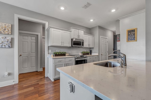 kitchen with sink, dark wood-type flooring, white cabinetry, stainless steel appliances, and light stone counters