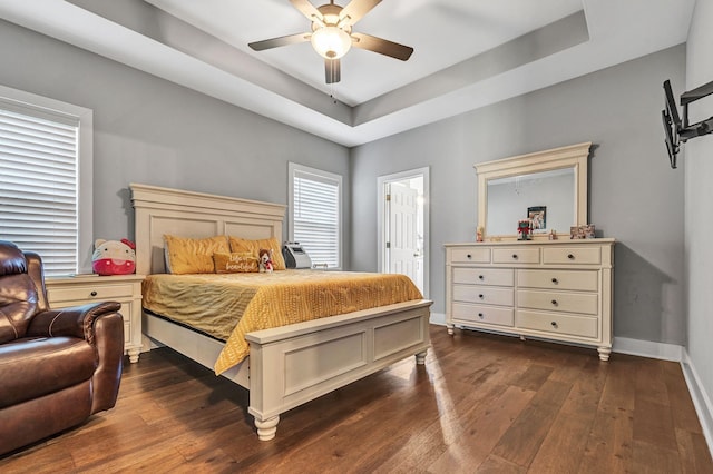 bedroom with dark hardwood / wood-style floors, ceiling fan, and a tray ceiling