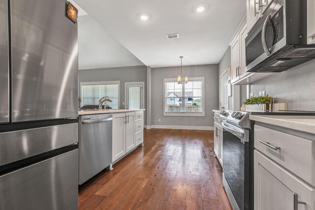 kitchen with sink, white cabinetry, appliances with stainless steel finishes, dark hardwood / wood-style floors, and pendant lighting