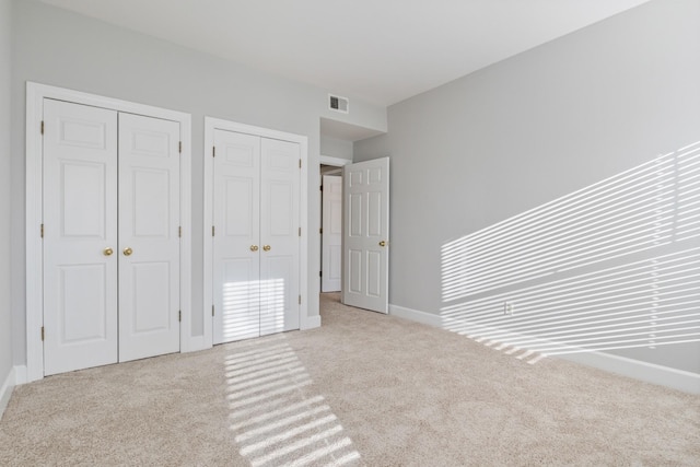 unfurnished bedroom with two closets and light carpet