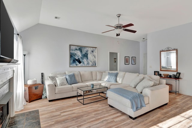 living room featuring ceiling fan, a fireplace, vaulted ceiling, and light hardwood / wood-style flooring