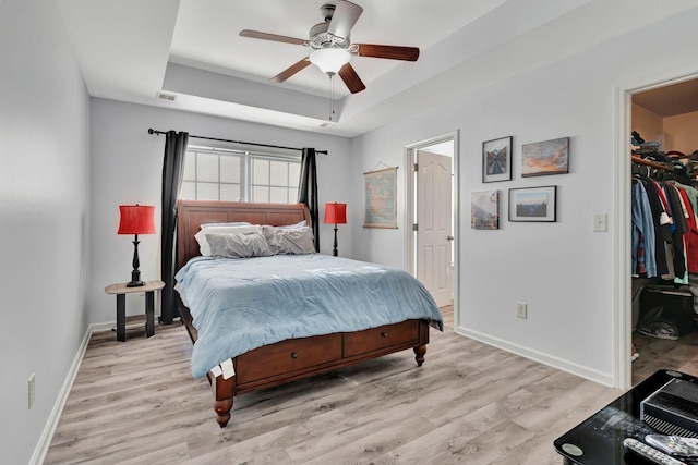 bedroom featuring a closet, a spacious closet, light wood-type flooring, and a tray ceiling