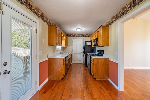 kitchen featuring sink, a textured ceiling, light hardwood / wood-style floors, and black appliances