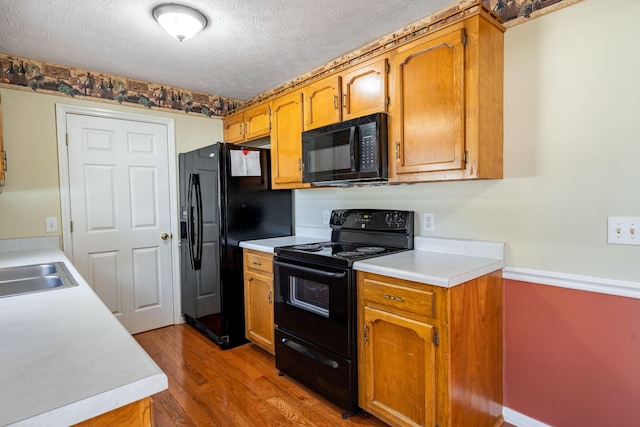 kitchen featuring wood-type flooring, sink, a textured ceiling, and black appliances