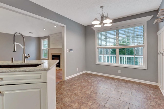 kitchen featuring sink, decorative light fixtures, a textured ceiling, a notable chandelier, and light stone countertops