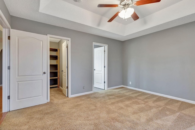 unfurnished bedroom featuring a spacious closet, light colored carpet, a textured ceiling, a tray ceiling, and ceiling fan