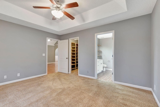 unfurnished bedroom featuring ensuite bathroom, a walk in closet, a tray ceiling, light carpet, and a closet