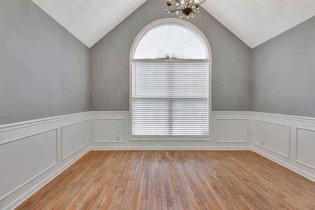 unfurnished room featuring lofted ceiling, light hardwood / wood-style floors, a textured ceiling, and a notable chandelier