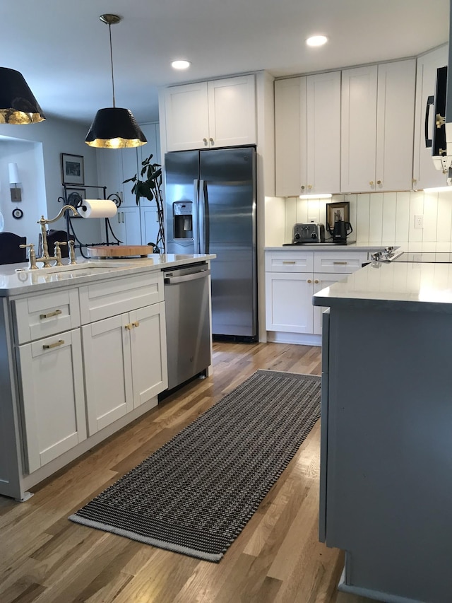 kitchen with stainless steel appliances, hanging light fixtures, white cabinets, and light hardwood / wood-style floors