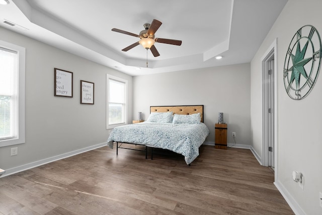 bedroom with hardwood / wood-style floors, a raised ceiling, and ceiling fan