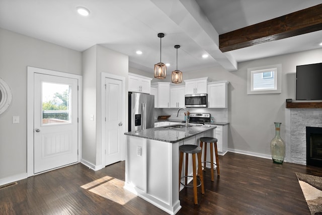 kitchen with sink, hanging light fixtures, appliances with stainless steel finishes, dark stone counters, and white cabinets