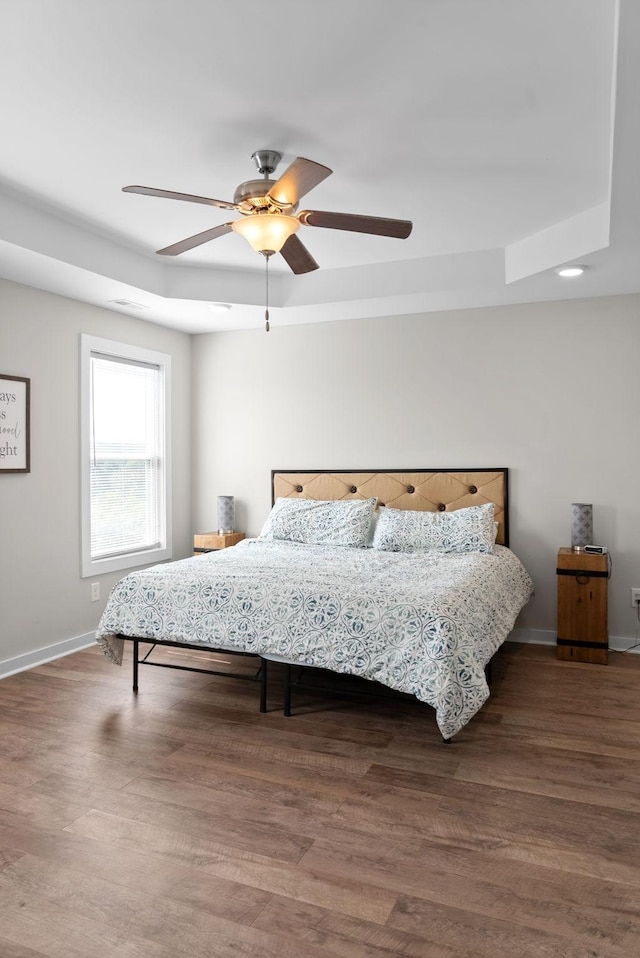 bedroom featuring hardwood / wood-style flooring, ceiling fan, and a raised ceiling