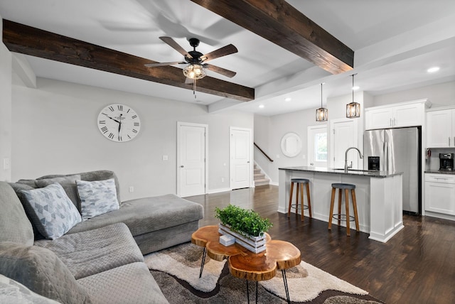 living room with ceiling fan, dark wood-type flooring, sink, and beamed ceiling